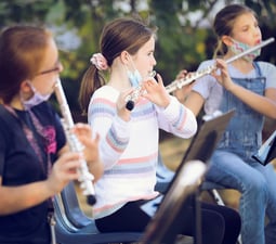 Middle school students play their flutes at an outdoor concert.