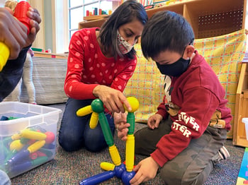 PreK teacher works with student to build a structure with magnetic toys